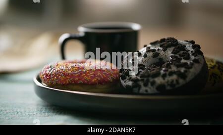View of assortment colorful frosted delicious tasty glazed sprinkled doughnuts on a table with a fresh hot coffee delicious breakfast donuts Stock Photo