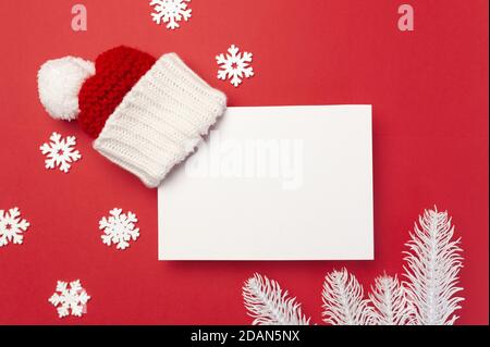 Greeting card mock up template with Christmas decorations red hat, white branches of fir tree and snowflakes on red background. Top View Stock Photo