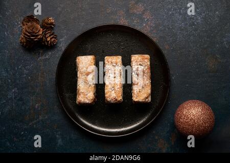 Stollen bars on a black plate surrounded by Christmas decorations Stock Photo