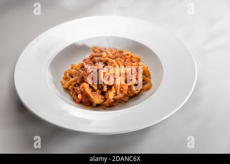 spaghetti egg based (Italian tagliatelle) topped with meat and tomato sauce, steamed in a plate on white background Stock Photo