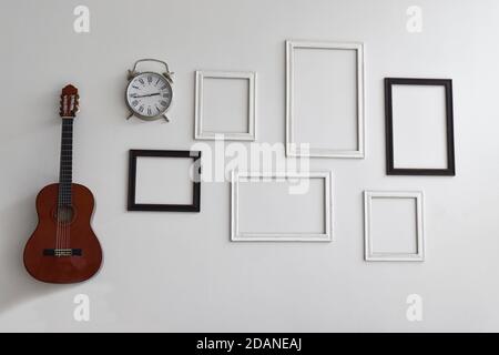 Blank picture frames, clock and guitar on white cement wall. Stock Photo