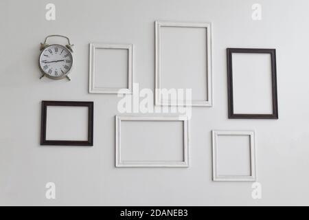 Blank picture frames and clock on white cement wall. Stock Photo