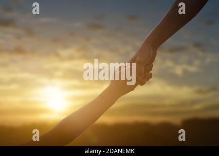 Silhouette of giving a help hand, hope and support each other over sunset background. Concept of helping hands and develop a friendship. Stock Photo