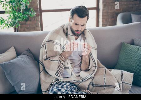 Portrait of his he nice attractive ill guy feeling bad sick leave sitting on divan measuring temperature suffering catch cold winter season at modern Stock Photo