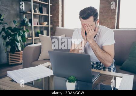 Portrait of his he nice attractive tired bored guy programmer digital specialist manager sitting on divan working remotely online overtime at modern Stock Photo