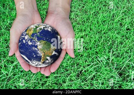 Earth day concept. Globe in hand on green lawn background. Elements of this image furnished by NASA Stock Photo