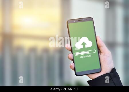 Close up of businessman hand holding mobile smartphone with cloud upload to store data on server. Stock Photo