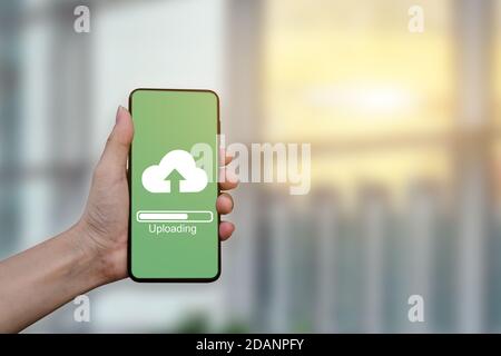 Close up of hand holding mobile smartphone with cloud upload to store data on server. Stock Photo
