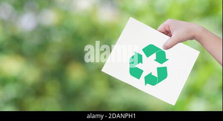 Child hand holding cut paper with logo recycling over green background. Concept of save environment. Stock Photo
