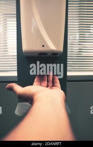 Male hand using automatic alcohol dispenser for cleaning hands in the office or hospital to sanitize virus and bacteria - Infection prevention concept Stock Photo