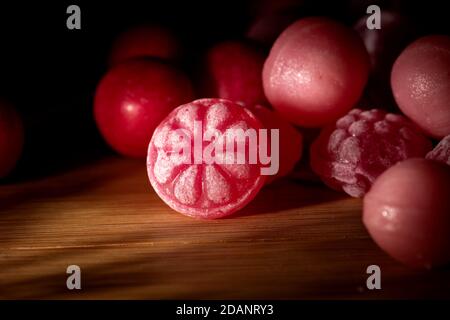 A dark portrait of some pieces of red and pink hard and round candy lying on a wooden table. The main piece of candy has a flower on it, others are ju Stock Photo