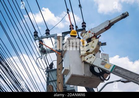 electricians in crane are working and installation of high voltage electric lines, transformer and telephone cables on pole in the city. Stock Photo