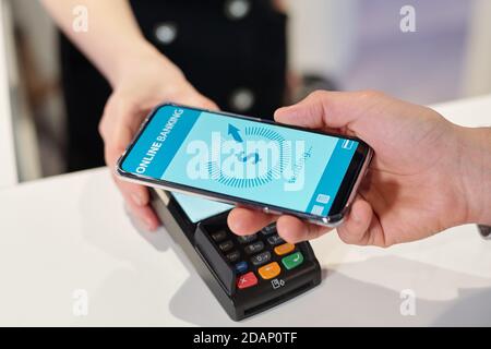 Hand of young man holding smartphone over terminal during contactless payment Stock Photo