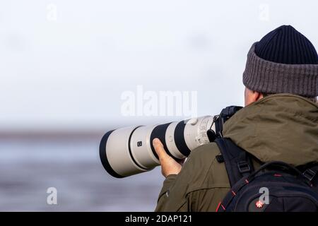 Photographer using a Sony camera and long G lens to photograph birds at RSPB Snettisham on a cold autumn day, UK