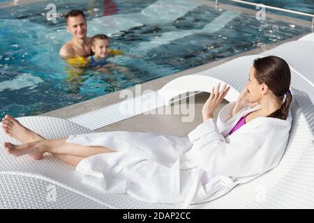 Young woman talking on smartphone and waving hand to her husband and daughter Stock Photo