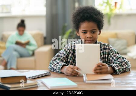 Cute elementary schoolboy of African ethnicity watching online lesson at home Stock Photo
