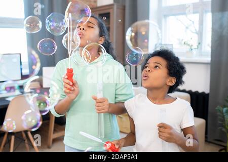 Cute siblings in casualwear blowing group of soap bubbles of various sizes Stock Photo