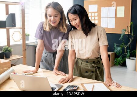 Two happy young businesswomen in casualwear watching video on laptop display Stock Photo