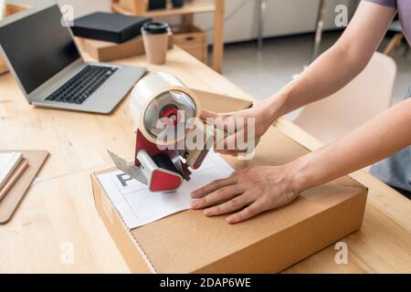 Hands of female manager of online shop sealing cardboard box with packed order Stock Photo