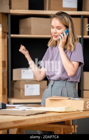 Young female manager of online shop calling one of clients after making order Stock Photo