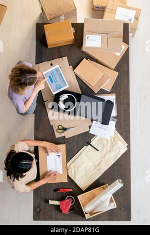 Top view of two young female managers checking online data and packing orders Stock Photo
