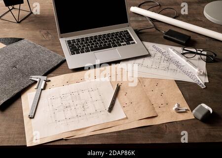 Laptop surrounded by blueprints with sketches of new building drawn by engineer Stock Photo