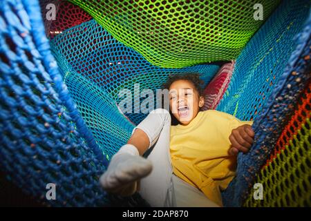 Excited African girl having fun in hammock in indoor amusement park Stock Photo