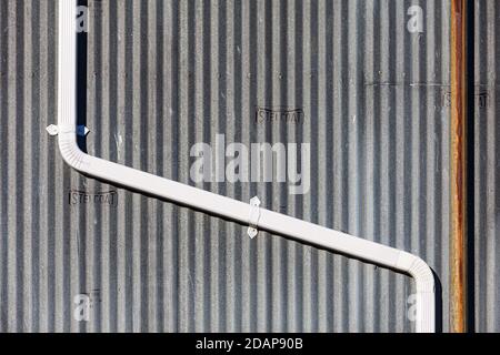 Abstract image of  a white downspout fastened to a corrugated external wall Stock Photo