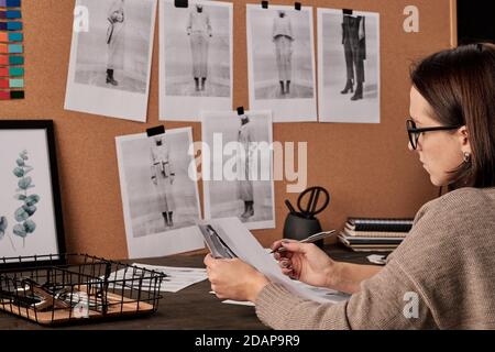 Young contemporary fashion designer working with photos by table in studio Stock Photo