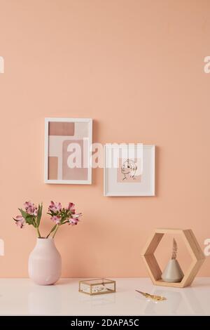 Two pictures in frames on pink wall by table with flowers in white ceramic vases Stock Photo
