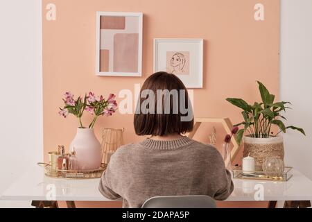 Back view of female interior designer sitting by table in front of pink wall Stock Photo