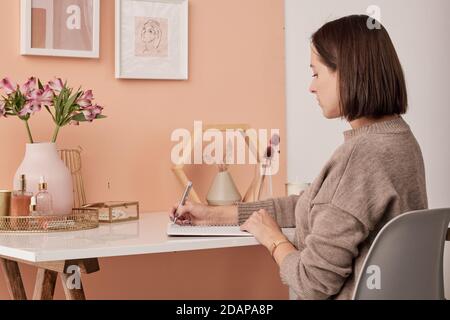 Young brunette female interior designer making working notes in copybook Stock Photo
