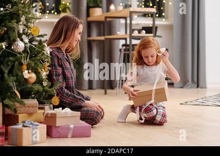 Cute little girl untying ribbon on giftbox while going to take out xmas present Stock Photo