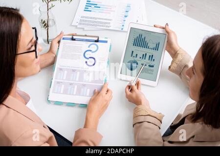 Two young businesswomen analyzing and discussing graph, charts and diagrams Stock Photo
