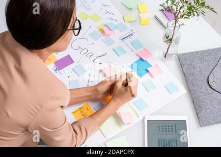 Young brunette businesswoman making notes on notepaper over large document Stock Photo