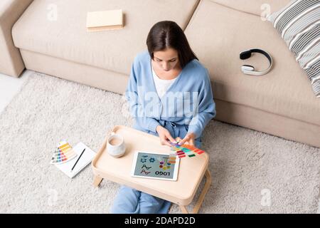 Young brunette female designer in blue pajamas choosing colors for new logo Stock Photo