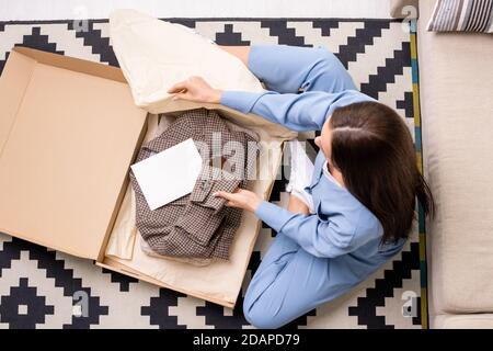 View of young woman packing checkered jacket from online shop into paper sack Stock Photo