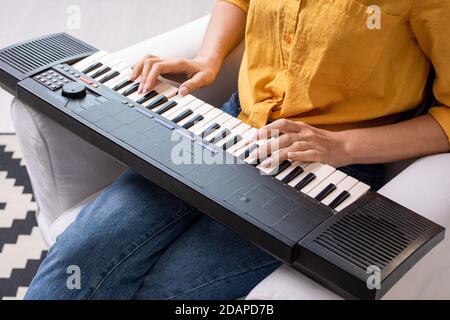 Hands of young woman in casualwear pressing keys of musical synthesizer keyboard Stock Photo
