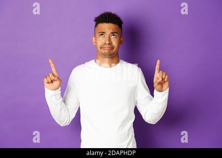 Skeptical and disappointed african-american male student, complaining, looking and pointing fingers up at something bad, grimacing dissatisfied Stock Photo
