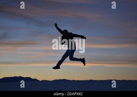 Young energetic happy man jumping high on mountain background and colorful sunset clouds pattern Stock Photo