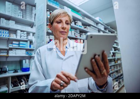 Caucasian senior pharmacist checking medication prescriptions on digital tablet standing in pharmacy  Stock Photo
