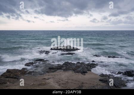 Seascape on a cloudy day with strong waves breaking and foaming against the rocks. Stock Photo