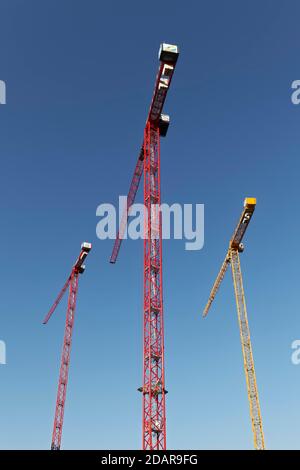 Two red construction cranes and a yellow construction crane in front of a blue sky, Germany Stock Photo