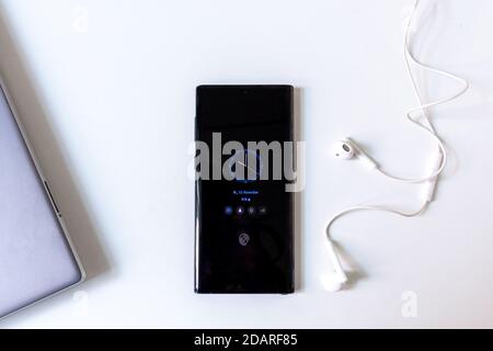 Black smartphone with digital blue clock and white earphones laying on the white office desk Stock Photo