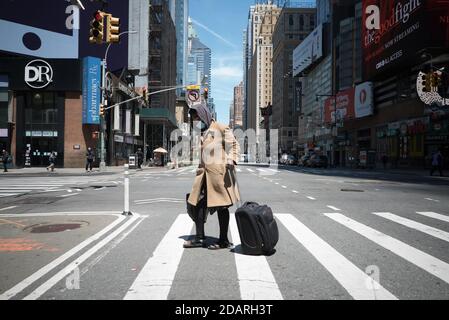 May 20, 2020. Manhattan, New York, Usa. A woman wearing a face mask with her luggage crosses an empty 8th avenue. Stock Photo