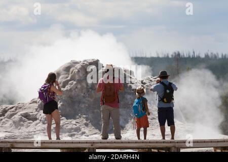 A family stops to take photos of Castle Geyser along the Upper Geyser Basin Trail in Yellowstone National Park, Wyoming on Monday, August 3, 2020. The Stock Photo