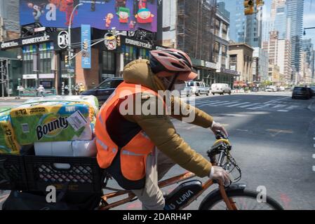 May 20, 2020. Manhattan, New York, Usa. A delivery man wearing a face mask rides a bicycle full of paper towels on an almost empty 8th avenue. Stock Photo