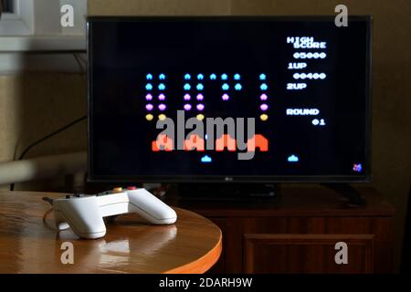 KHARKOV, UKRAINE - NOVEMBER 12, 2020: Dendy video game controller on table with Space invaders game on big display Stock Photo