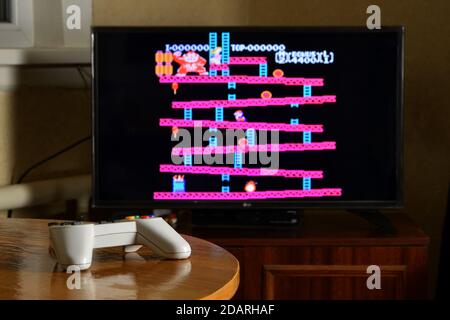 KHARKOV, UKRAINE - NOVEMBER 12, 2020: Dendy video game controller on table with Donkey Kong game on big display Stock Photo