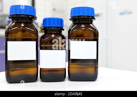 Selective focus of three dark glass reagent bottle with unknown clear liquid chemical inside and blank label in a chemistry laboratory. Stock Photo